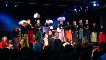 Stāstnieku festivāla Ziv zup koncertā Cik augšā sīku zvaigžņu, zemē sīku akmentiņu dalībnieki vienojas tautasdziesmā Upe nesa ozoliņu. Uz skatuves – Padures ansamblis Harmonija, centrā festivāla rīkotāja Ina Celitāne un mazā stāstniece Gerda Gruze.